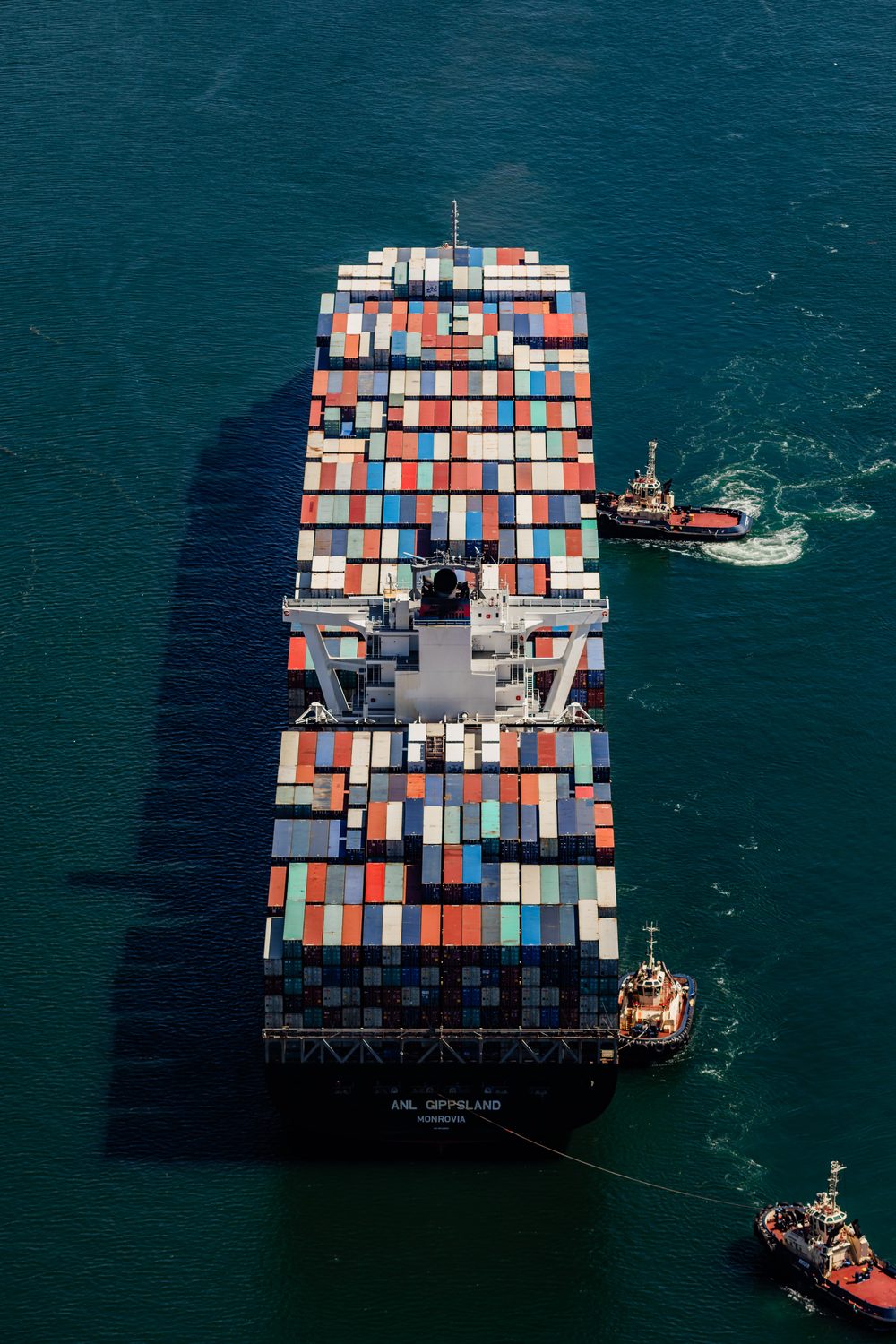 Aerial view of a fully loaded container ship named ANL Gippsland, registered in Monrovia, being guided into port by tugboats